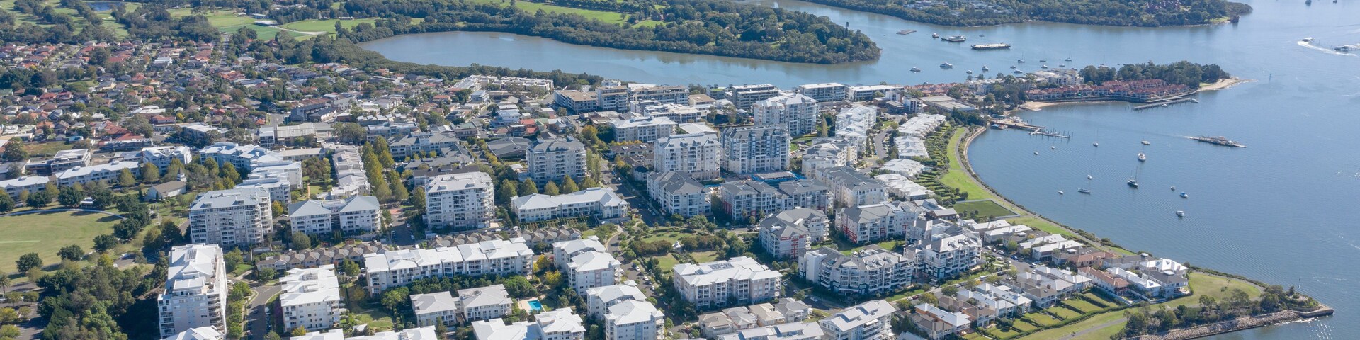 Vista aérea de uma área residencial costeira com edifícios de apartamentos modernos, um porto de iates e um rio.