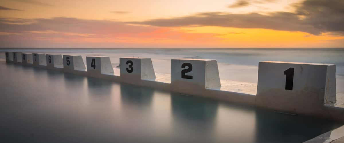 A series of numbered concrete blocks along a shoreline at sunset.
