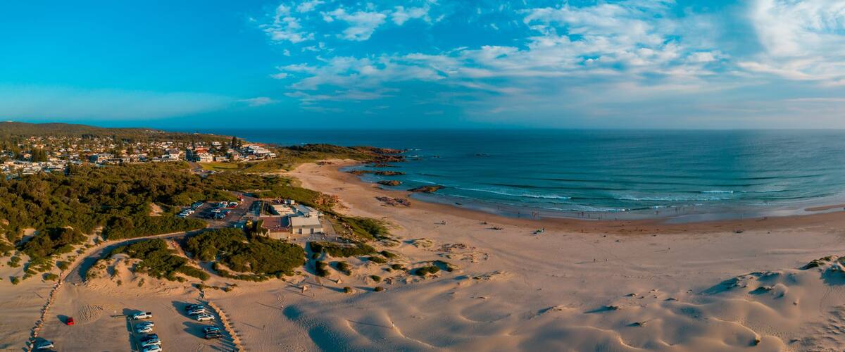 A coastal landscape with a sandy beach, a clear sky, and a distant town.