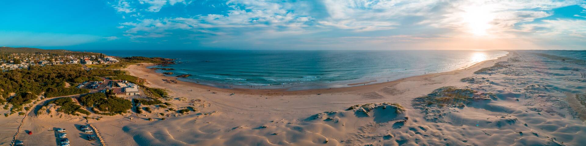 A coastal landscape with a sandy beach, a clear sky, and a distant town.