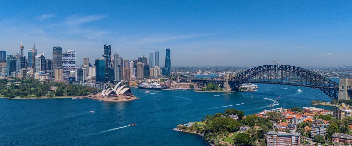 A city skyline with modern skyscrapers, a prominent bridge, and the Sydney Opera House.