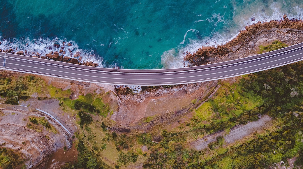 An aerial view of a coastal road with a bridge over the ocean.