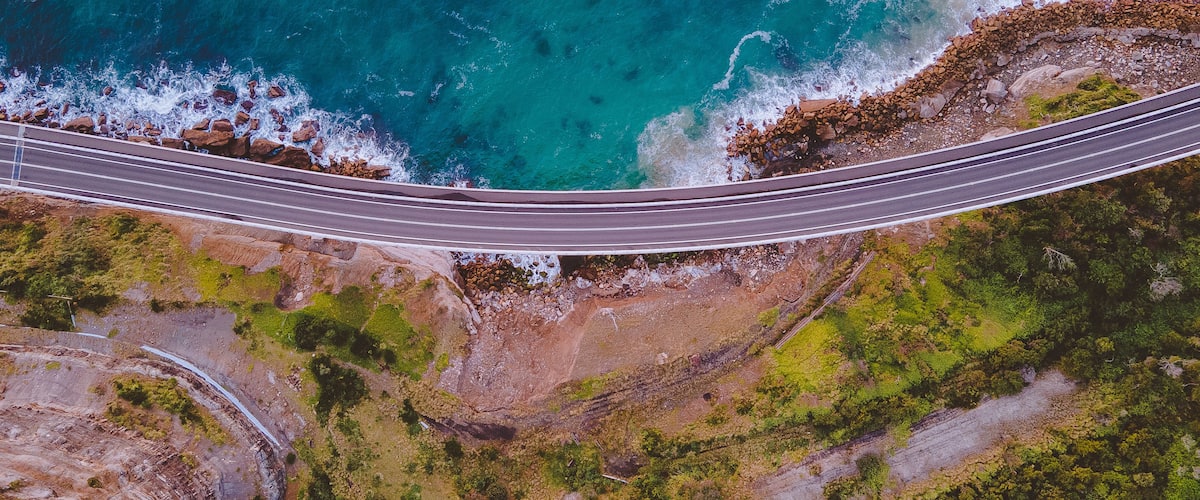 An aerial view of a coastal road with a bridge over the ocean.