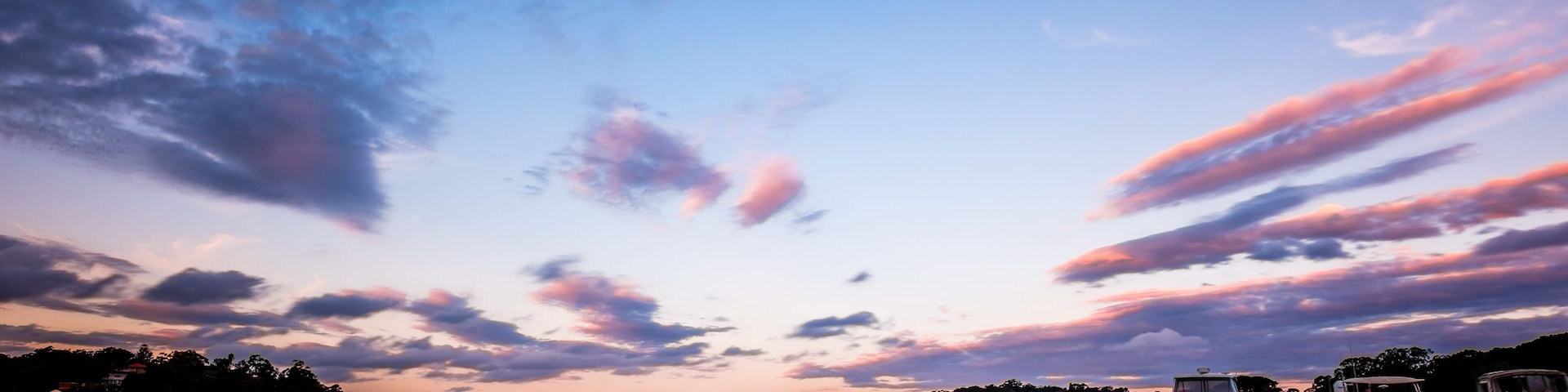 A calm harbor with boats at sunset, a clear sky, and a distant shoreline with buildings.