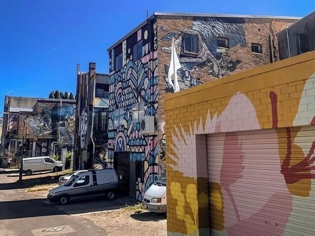 A building with colorful murals, a parked car, and a closed garage door.