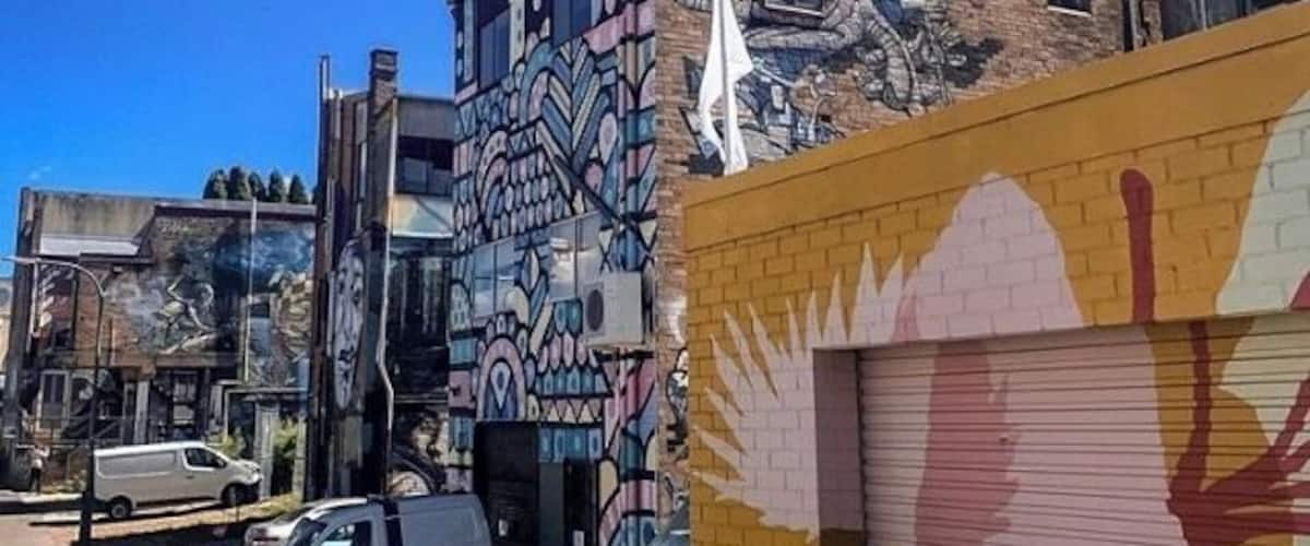 A building with colorful murals, a parked car, and a closed garage door.