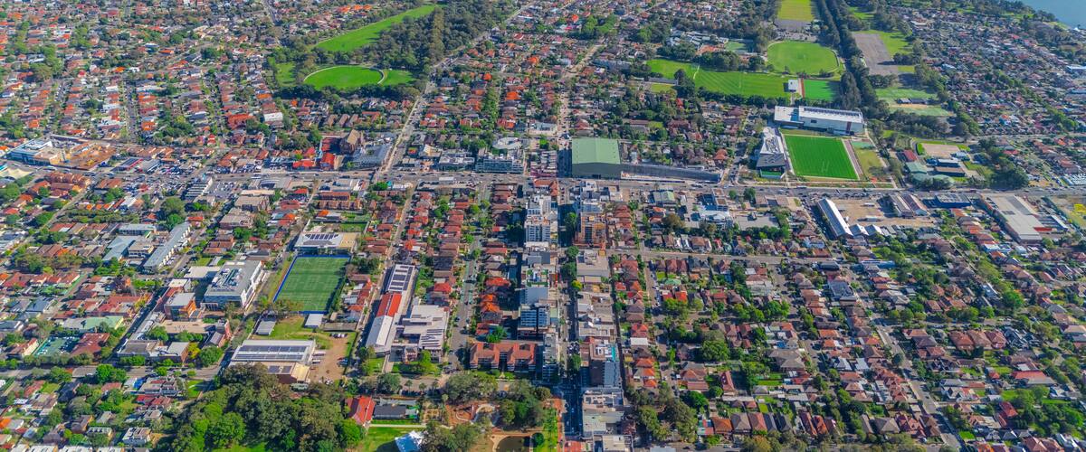 An aerial view of a densely populated urban area with residential buildings, green spaces, and a large body of water.