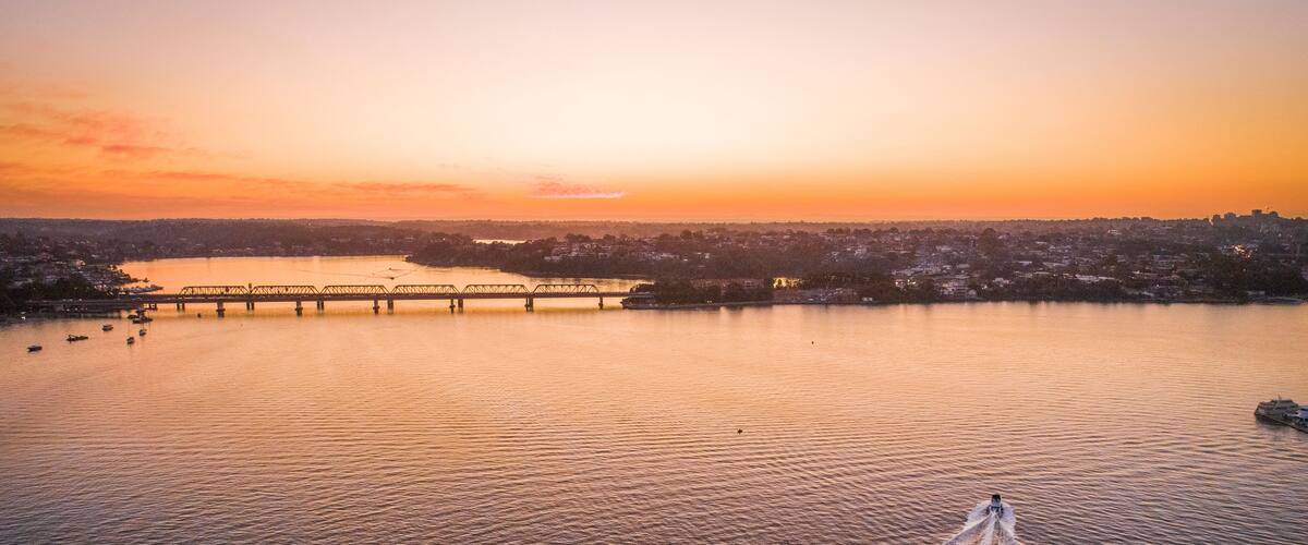 A sunset over a river with a bridge and a cityscape in the background.