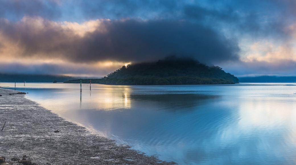 A calm lake with a small island in the center, surrounded by a cloudy sky.
