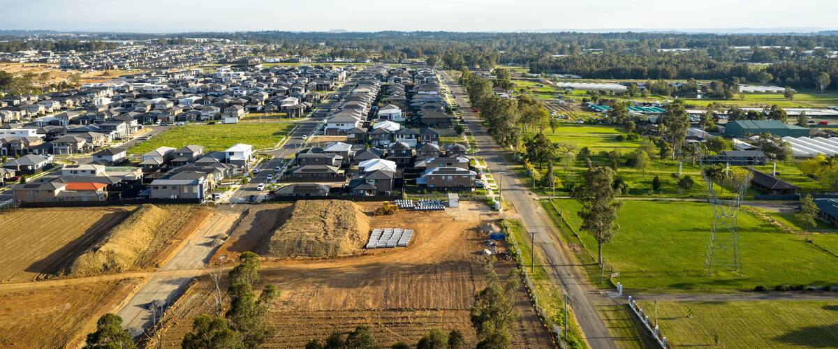 Área residencial com casas, estrada e campos agrícolas.