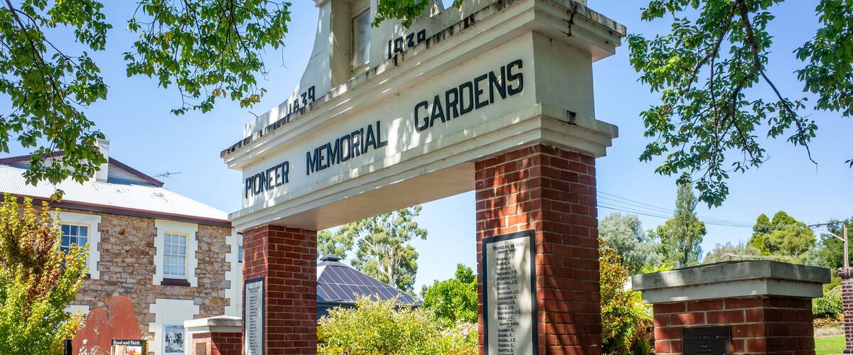 Pioneer Memorial Gardens entrance with a sign, brick pillars, and surrounding greenery.