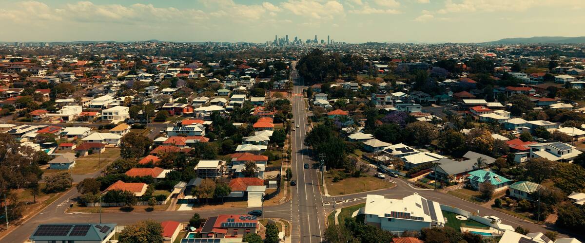 An aerial view of a residential area with houses, roads, and a distant city skyline.
