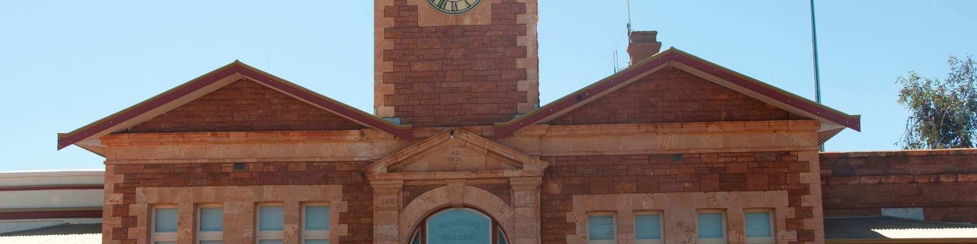 Uma prefeitura de tijolos com torre do relógio, entrada em arco e uma placa com a inscrição 'Town Hall'.