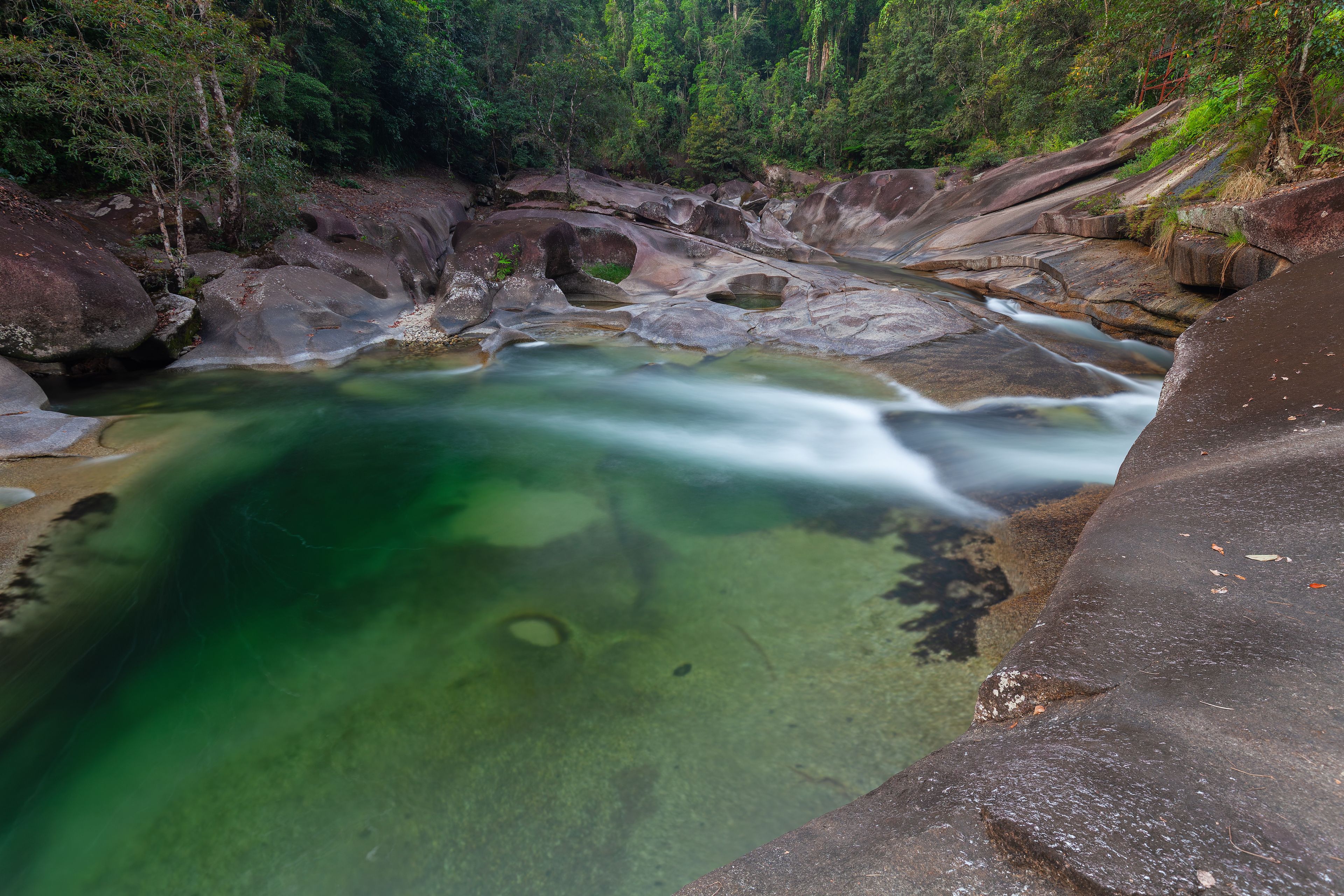 A clear, greenish stream flowing over rocks in a forested area.