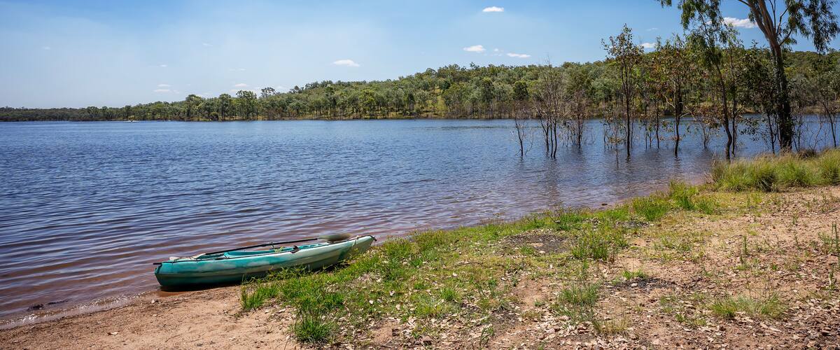 Un lago tranquillo con una canoa verde sulla riva, circondato da alberi e un cielo sereno.