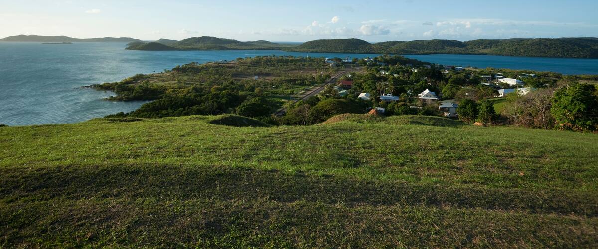 A coastal landscape with a small settlement by the sea, surrounded by hills and greenery.