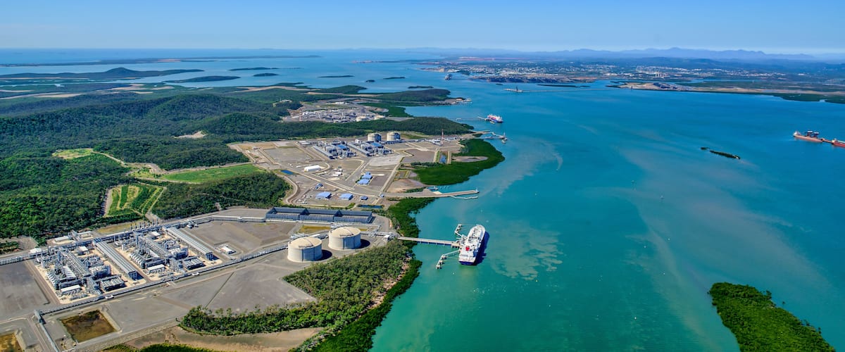 An industrial port with a large cargo ship docked, surrounded by water and greenery.