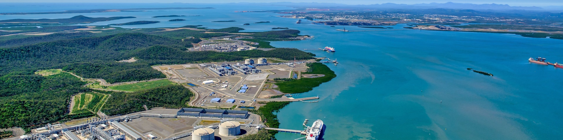 Un puerto industrial con un gran barco de carga atracado, rodeado de agua y vegetación.