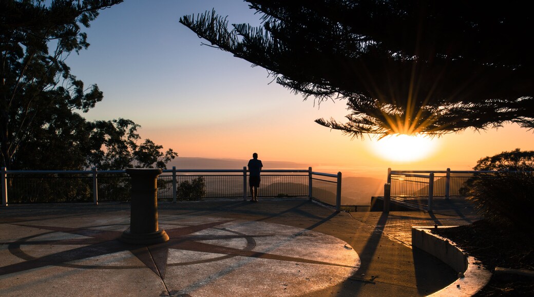 A sunset view from a park with a person standing on a viewing platform, overlooking a body of water.
