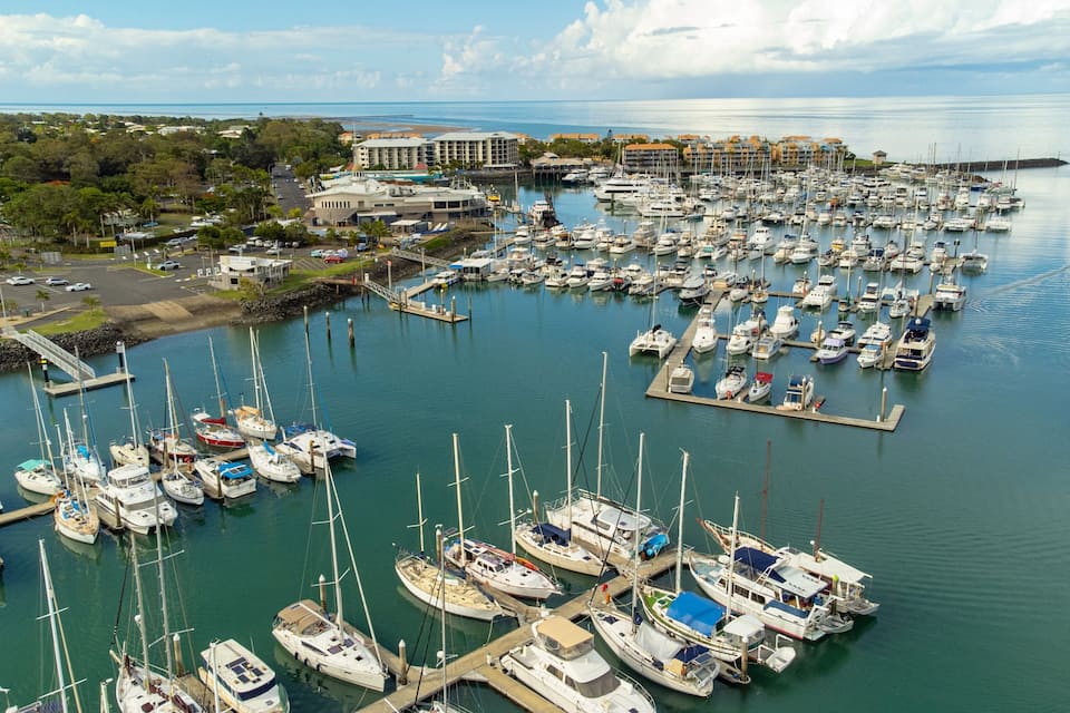 A marina with numerous boats docked, a bridge, and buildings in the background.