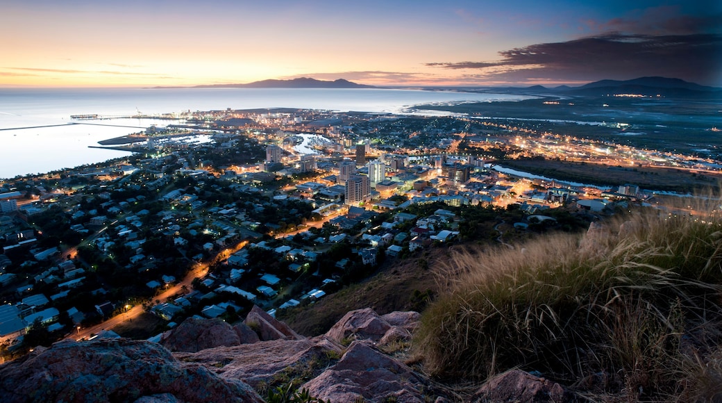 A coastal cityscape at dusk with a view of the ocean and mountains in the distance.