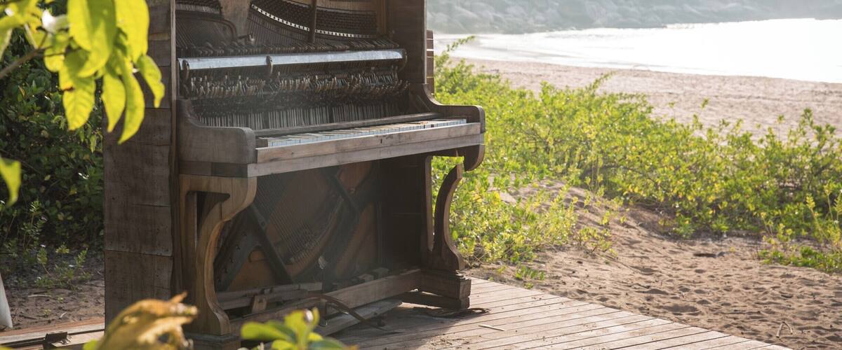 A grand piano on a wooden deck by the beach with a backdrop of hills and ocean.