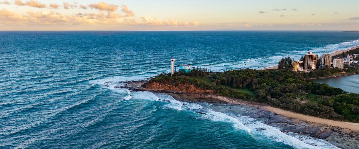 Paisagem costeira com um farol, praia e edifícios residenciais.