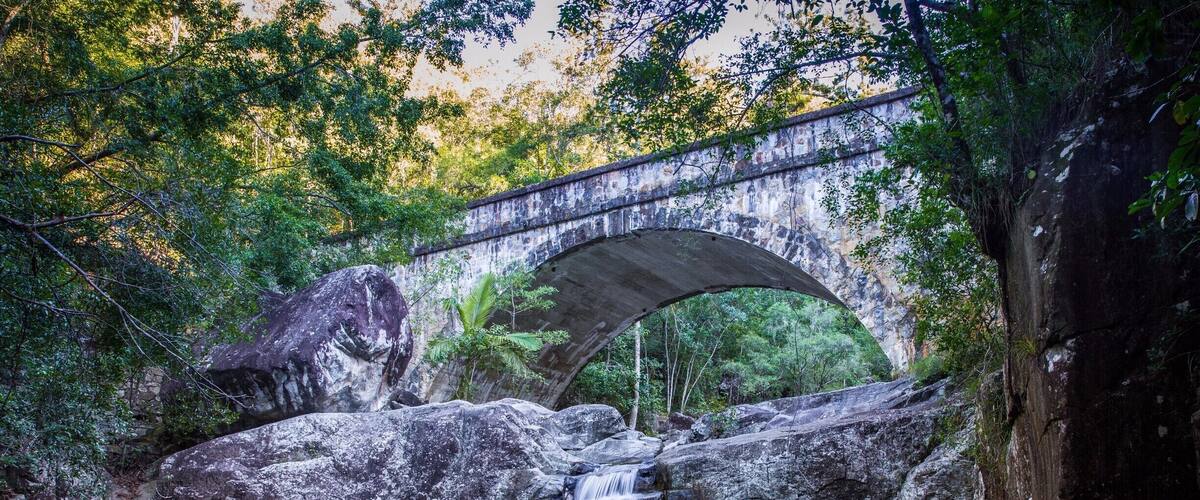 A waterfall under a stone bridge surrounded by rocks and trees.
