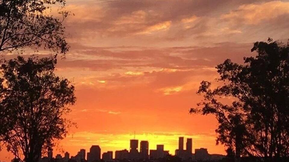 Ein Sonnenuntergang über einer Stadtlandschaft mit schattenhaften Gebäuden und Bäumen.