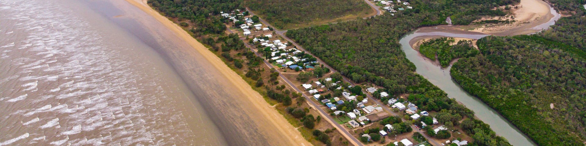 An aerial view of a coastal area with a beach, a river, and a residential area with houses.