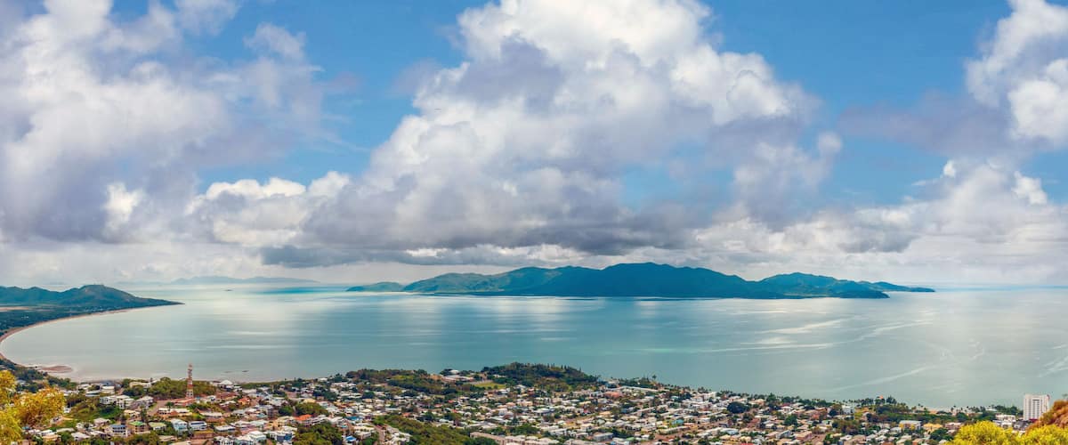 A coastal town with a bay, mountains in the distance, and a cloudy sky.