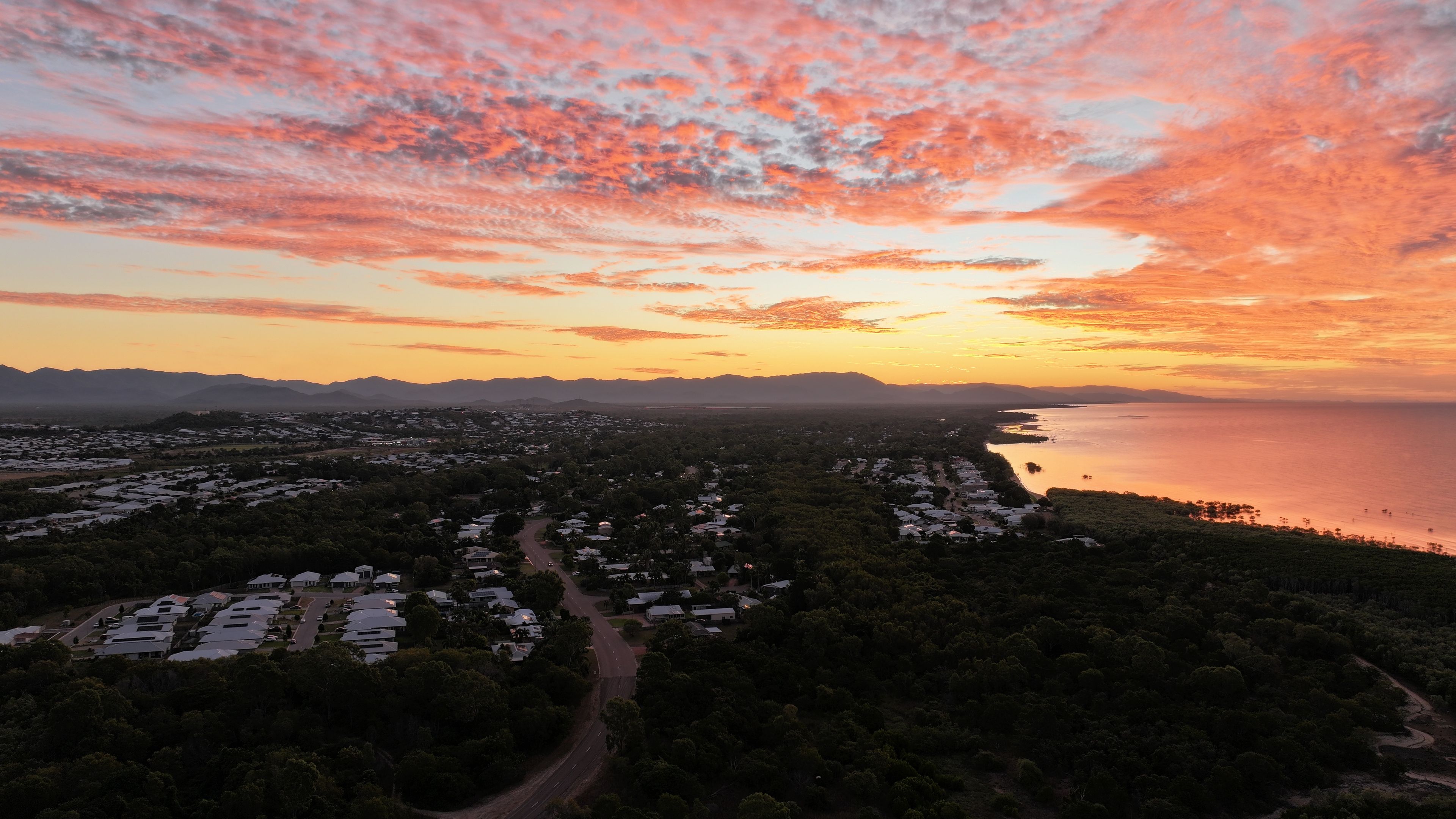A coastal landscape with a sunset, a road, and a cluster of buildings.