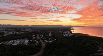 A coastal landscape with a sunset, a road, and a cluster of buildings.