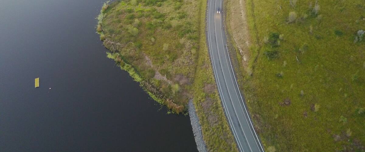 A winding road alongside a calm lake with grassy banks.