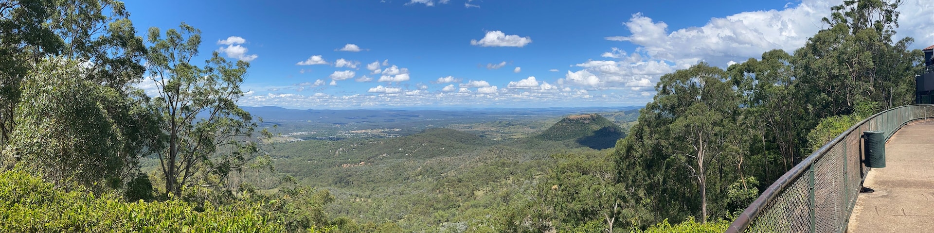 A scenic overlook with a view of a valley, dense greenery, and a clear blue sky.