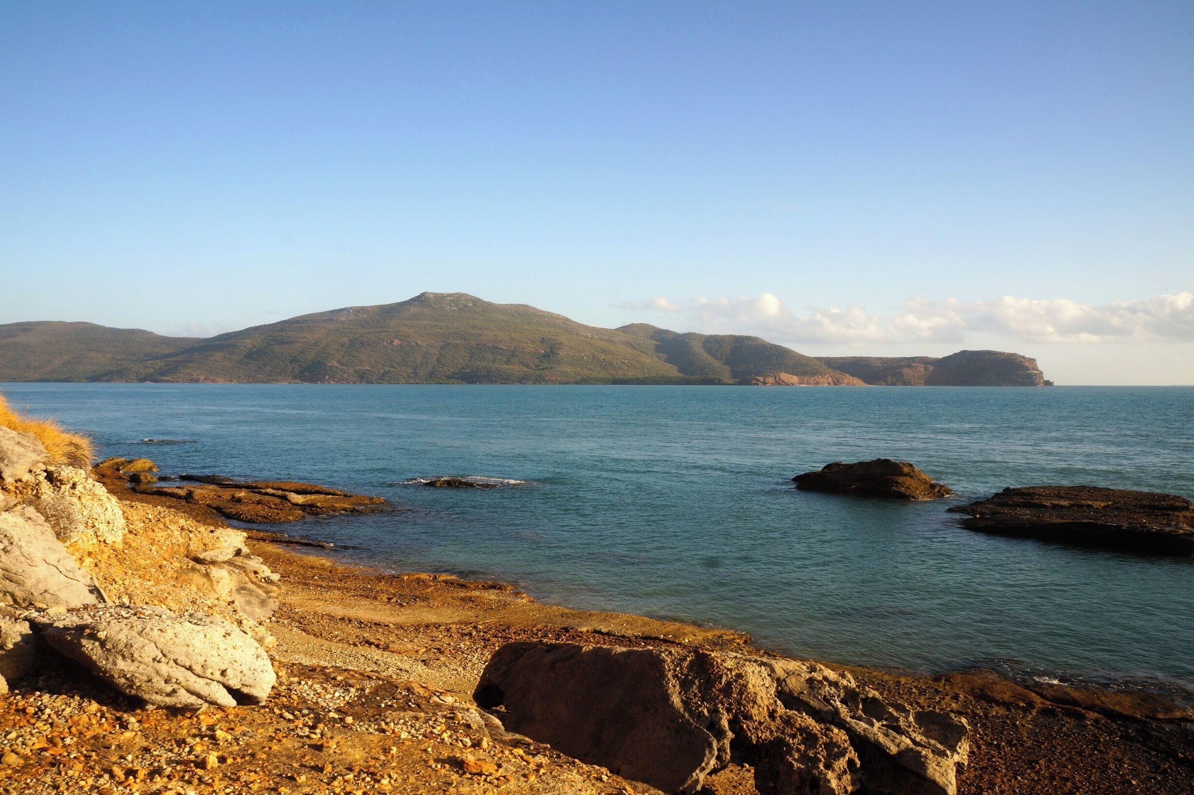 A coastal landscape with rocky shores, calm sea, and distant hills.