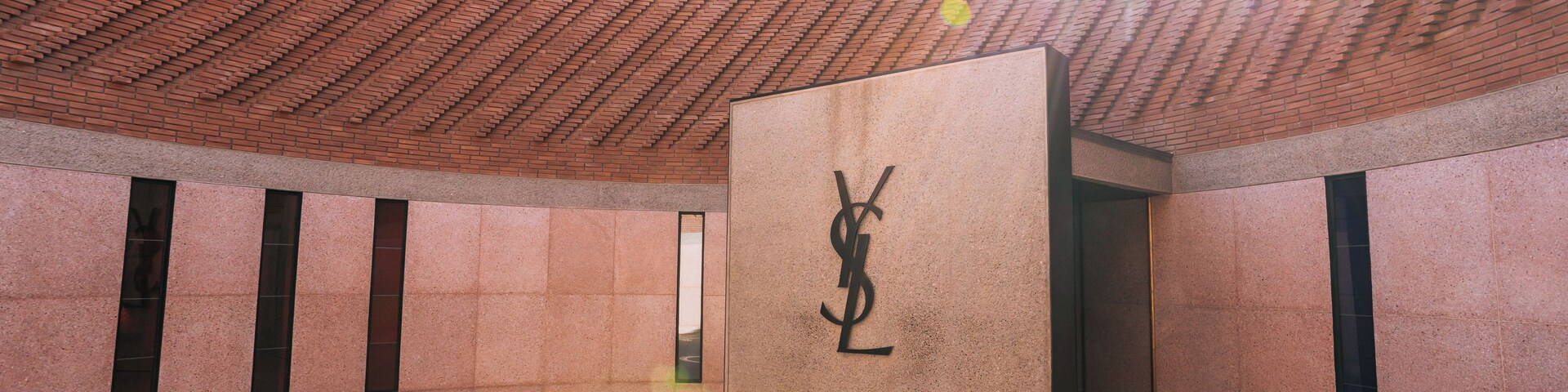 Um edifício moderno com telhado curvo de tijolos e o logotipo Yves Saint Laurent bem visível.