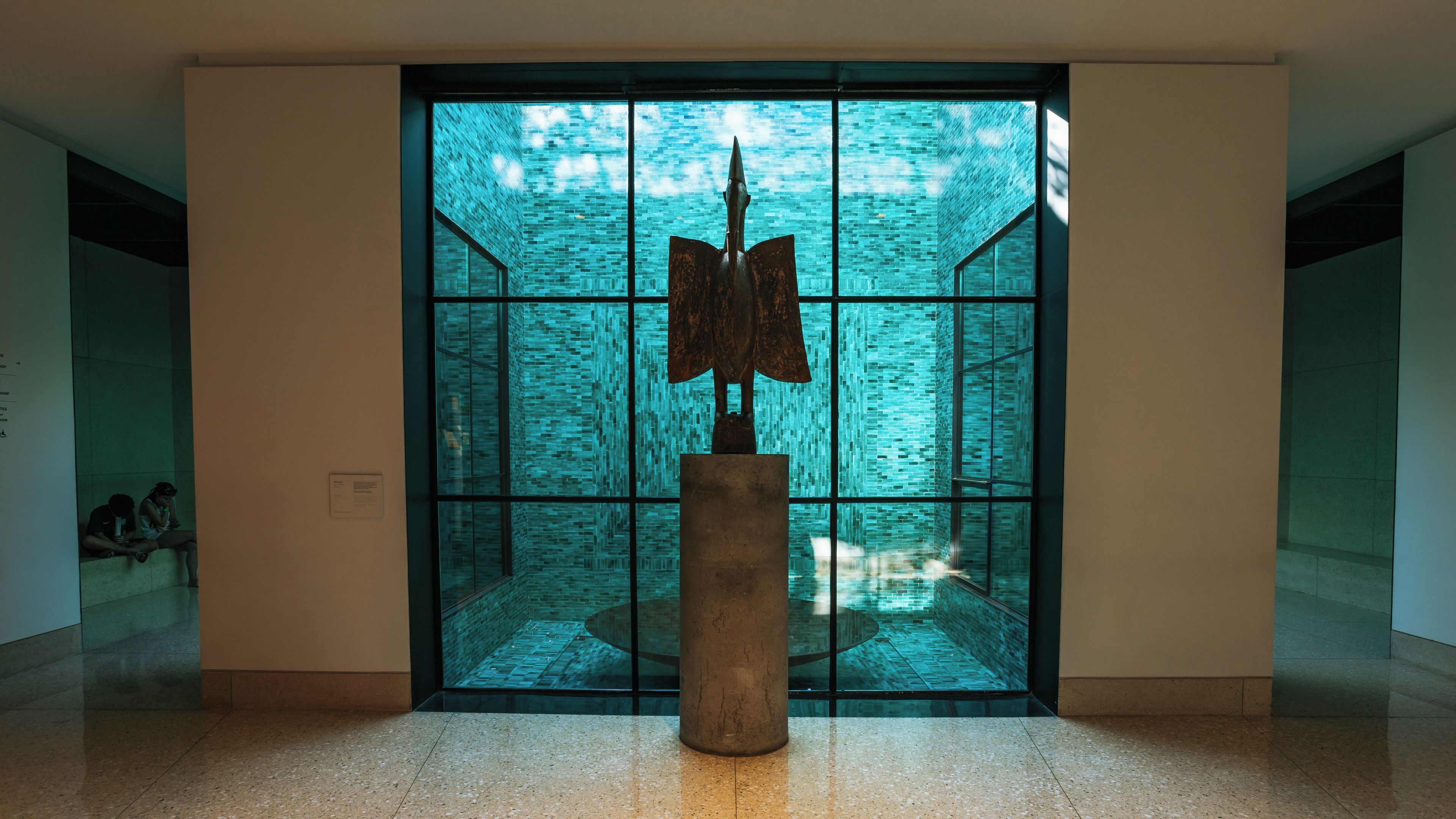 A modern interior space with a large glass window, a metal sculpture, and a tiled floor.