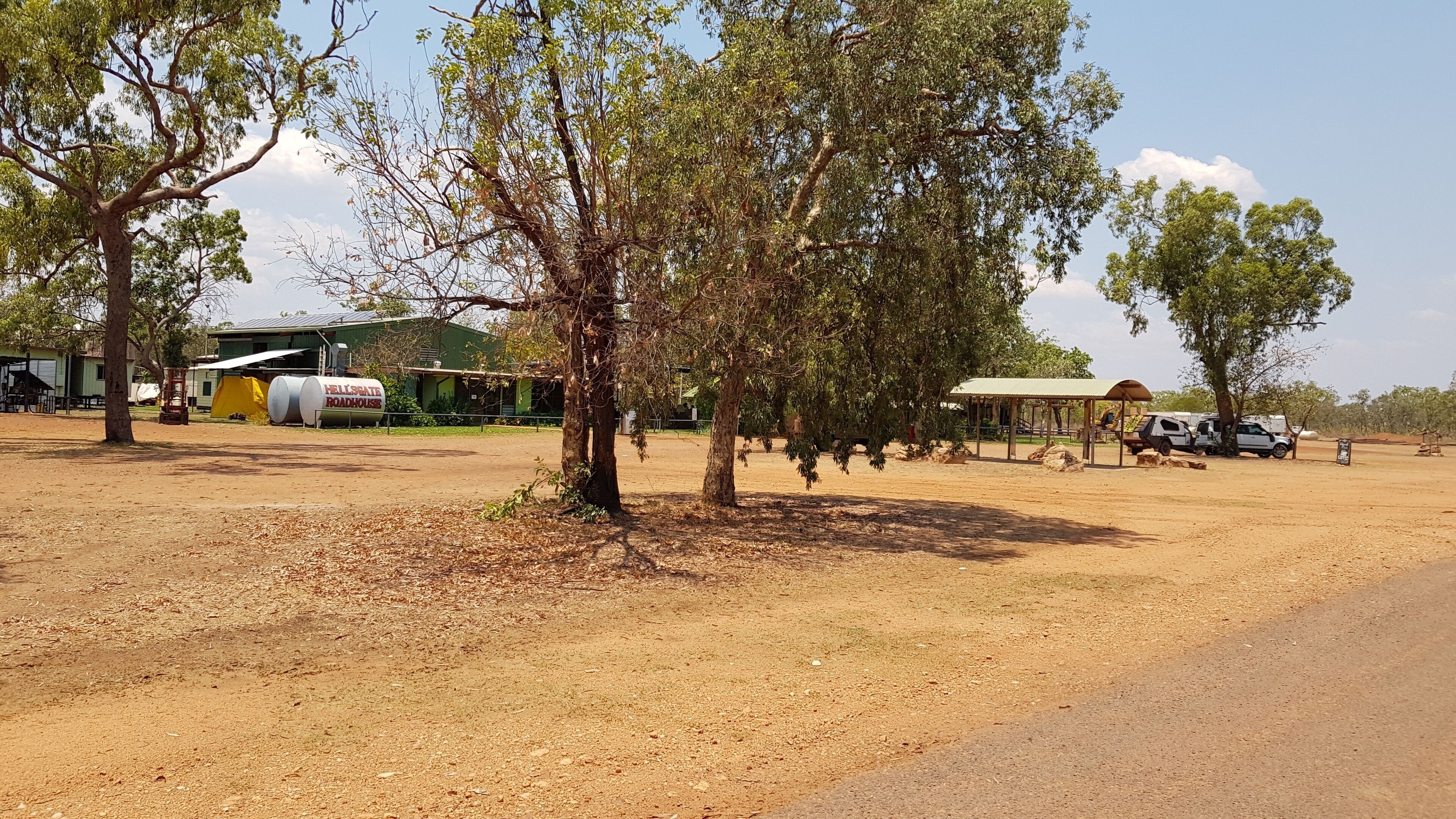 A rural landscape with trees, a roadhouse, and a few vehicles.