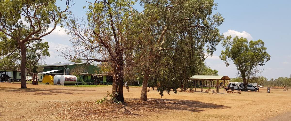 A rural landscape with trees, a roadhouse, and a few vehicles.