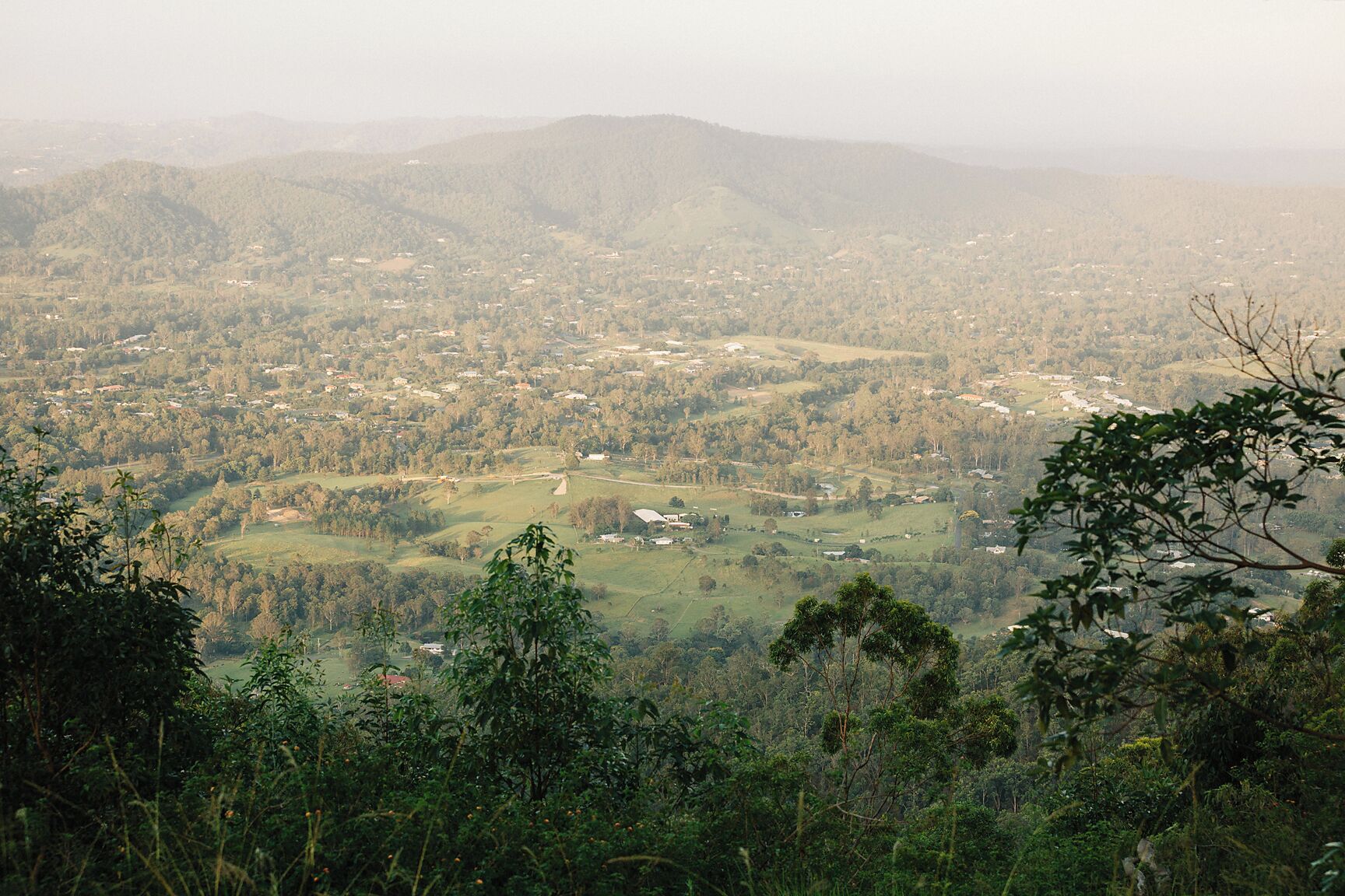 A panoramic view of a hilly landscape with scattered houses and dense forested areas.