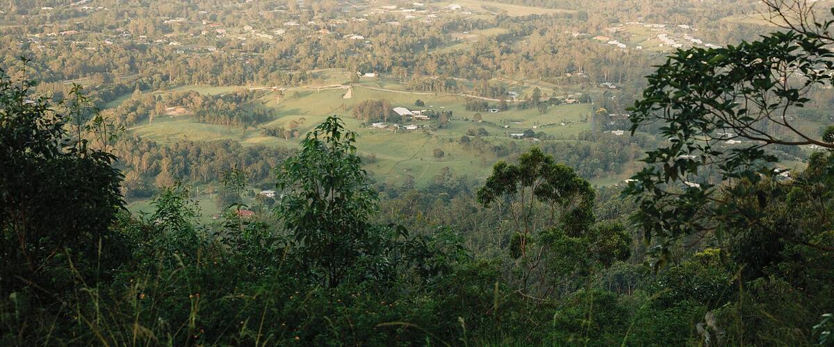 A panoramic view of a hilly landscape with scattered houses and dense forested areas.