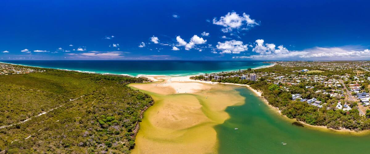 A coastal landscape with a river, beach, and residential area.