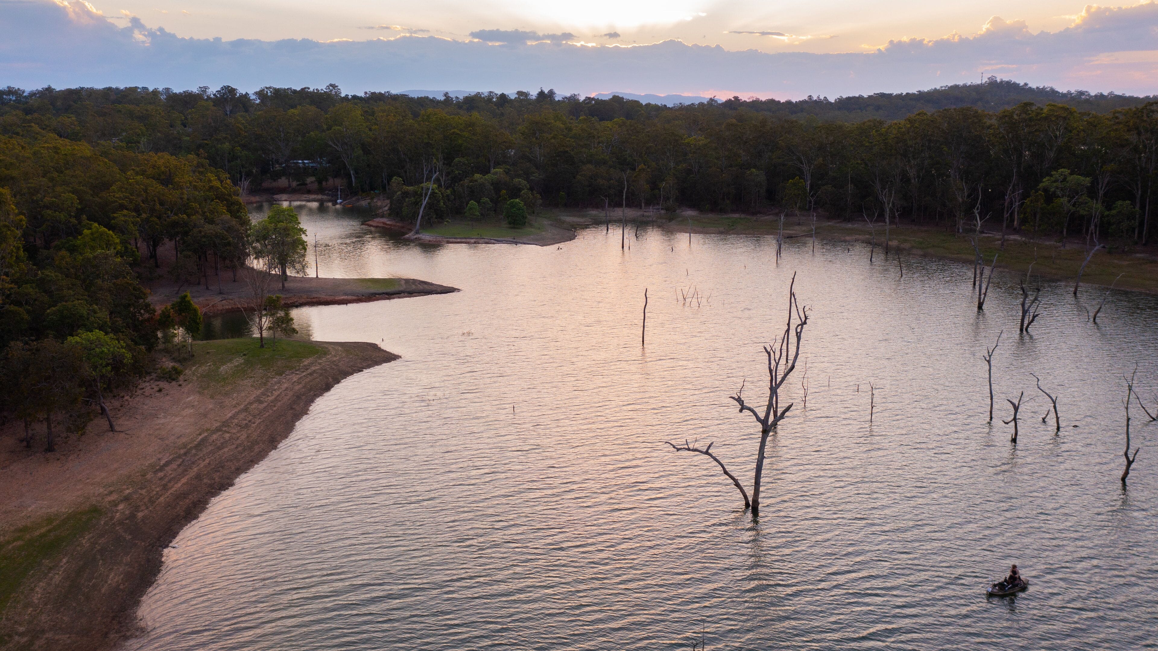 A river with a boat, surrounded by trees and a hilly landscape.