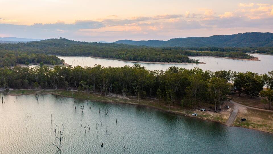 A lake surrounded by forested hills and a road with vehicles.