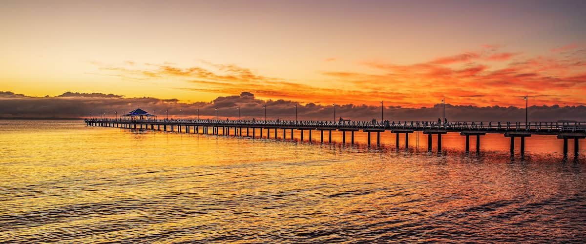 A pier extending into a body of water during sunset with a clear sky.