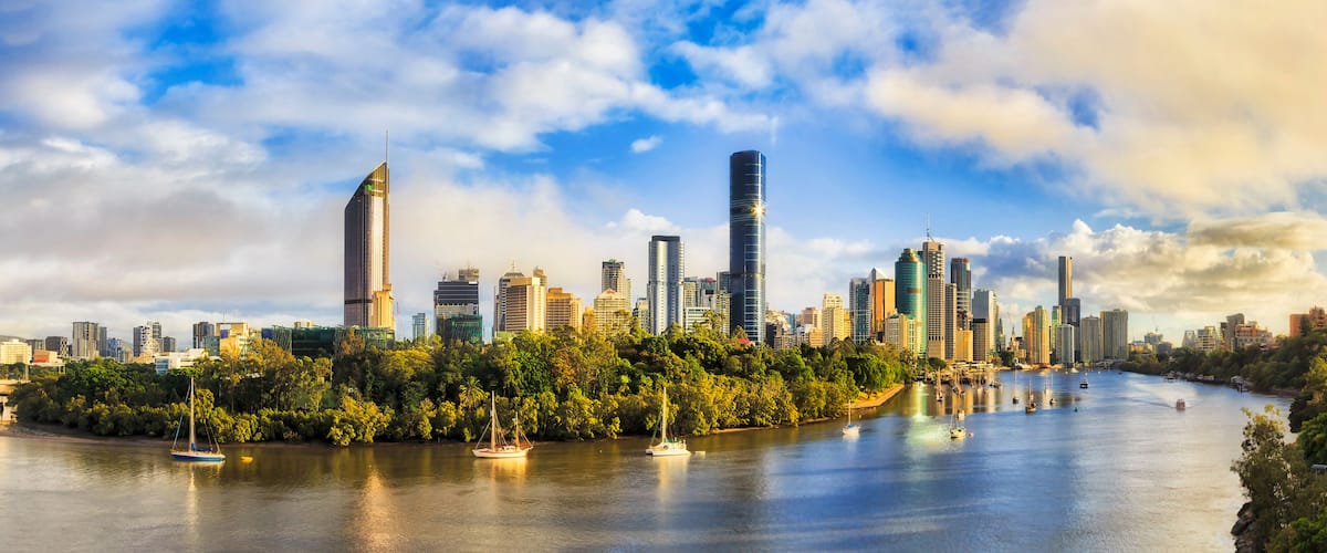 A city skyline with modern skyscrapers, a river with boats, and lush greenery along the riverbanks.