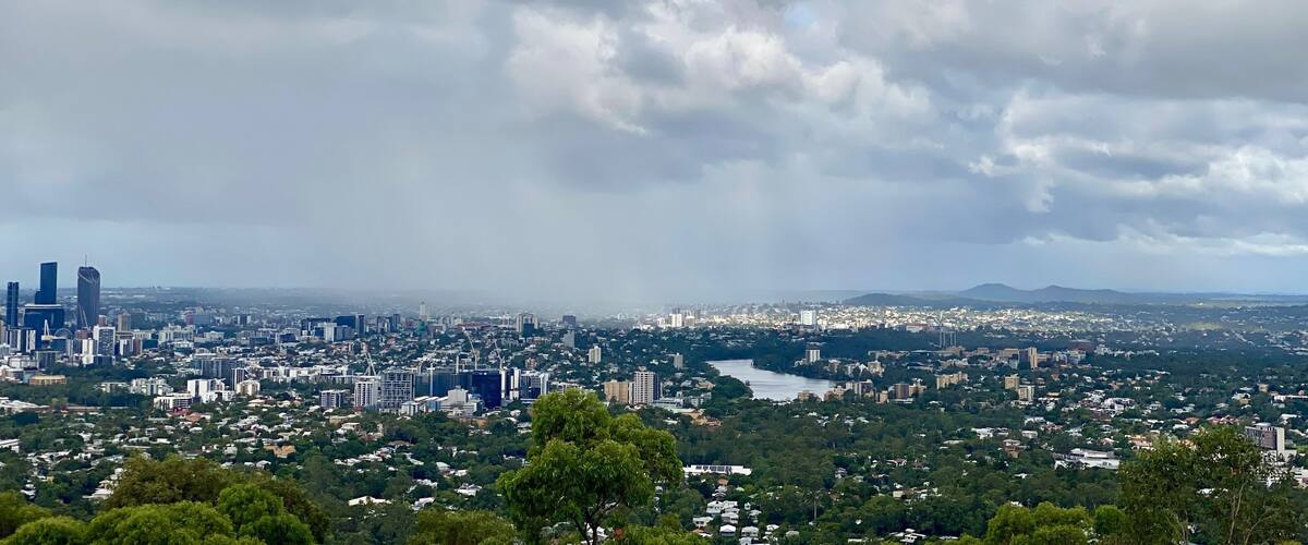A cityscape with a river, dense greenery, and a cloudy sky.