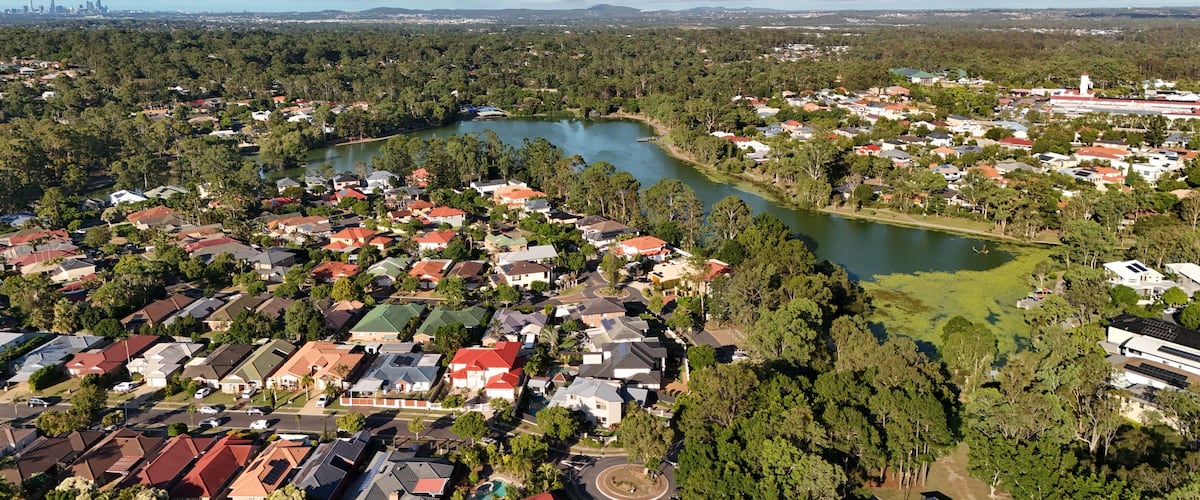 A residential area with houses, a river, and a distant city skyline.