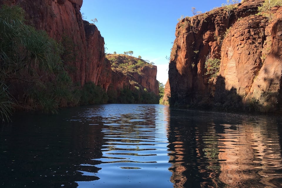 A river canyon with steep red rock walls and sparse vegetation.